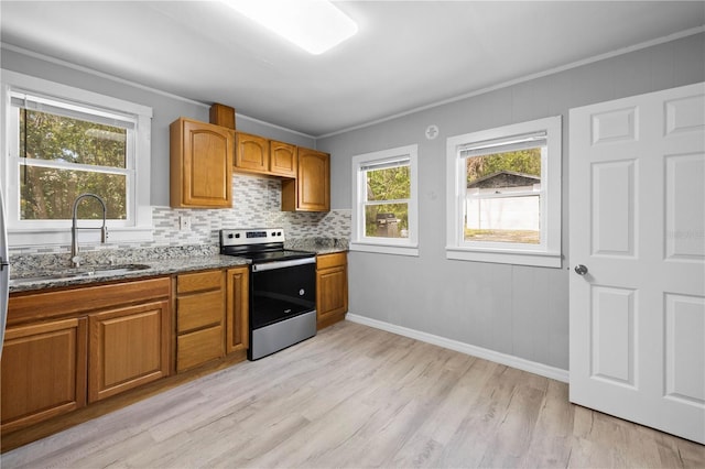 kitchen with dark stone counters, decorative backsplash, stainless steel range with electric stovetop, brown cabinetry, and a sink