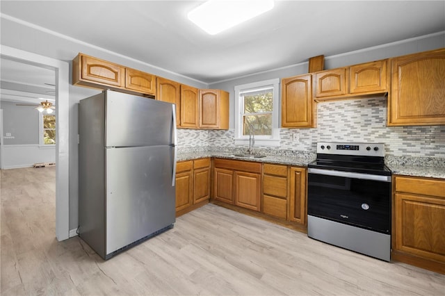 kitchen with brown cabinetry, a sink, light wood-style floors, appliances with stainless steel finishes, and backsplash