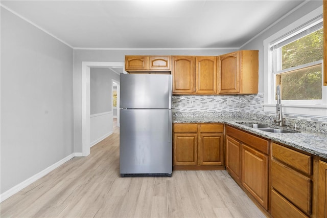 kitchen featuring light wood-type flooring, a sink, freestanding refrigerator, decorative backsplash, and light stone countertops