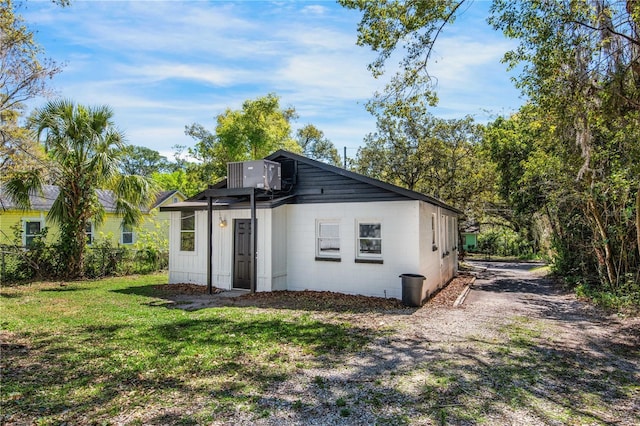 rear view of property featuring central AC unit, concrete block siding, and a yard