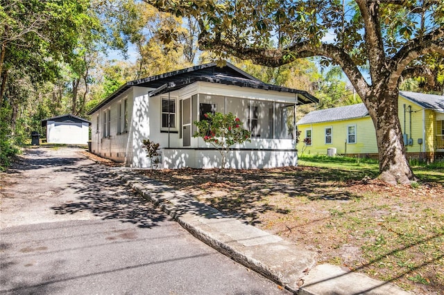 bungalow-style home featuring aphalt driveway, central air condition unit, an outbuilding, and a sunroom