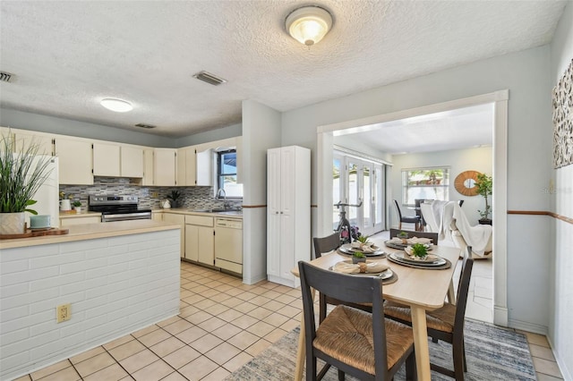 kitchen featuring dishwasher, light countertops, light tile patterned floors, stainless steel range with electric stovetop, and fridge