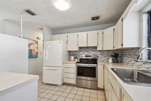 kitchen featuring visible vents, freestanding refrigerator, a sink, light countertops, and electric stove