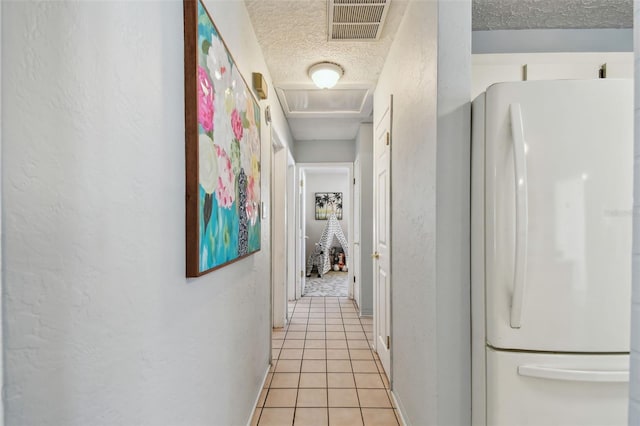 corridor featuring light tile patterned floors, visible vents, attic access, a textured ceiling, and a textured wall