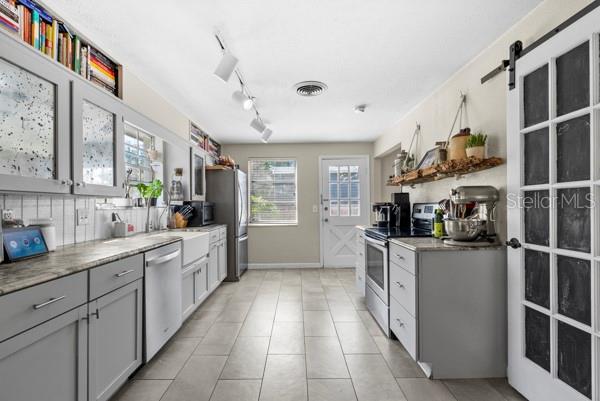 kitchen featuring gray cabinetry, stainless steel appliances, visible vents, decorative backsplash, and open shelves