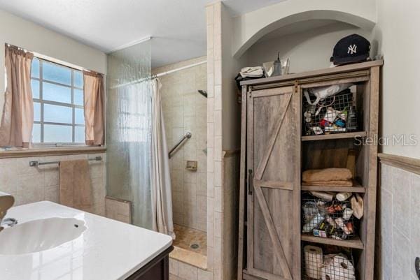 bathroom with vanity, wainscoting, a shower stall, and tile walls