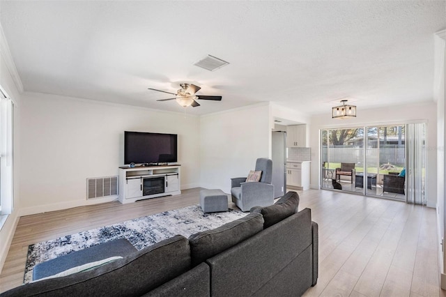 living area with light wood-type flooring, a fireplace, visible vents, and crown molding