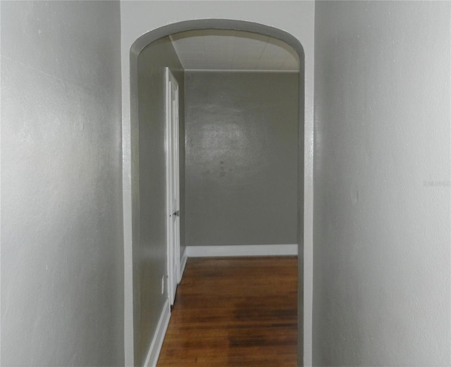 hallway with arched walkways, baseboards, and wood finished floors