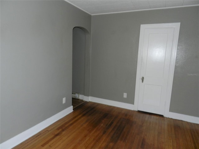 spare room with arched walkways, baseboards, and hardwood / wood-style flooring