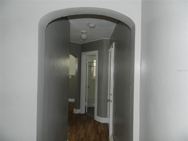 hallway with arched walkways, baseboards, and wood finished floors