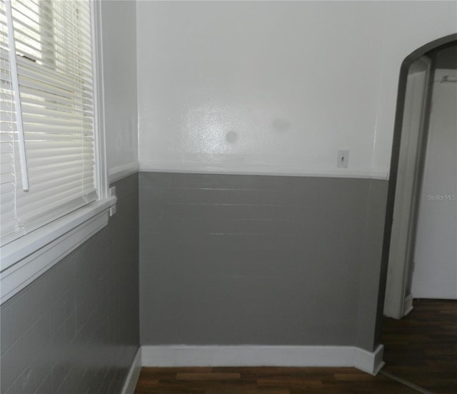 spare room featuring arched walkways, dark wood-type flooring, and baseboards