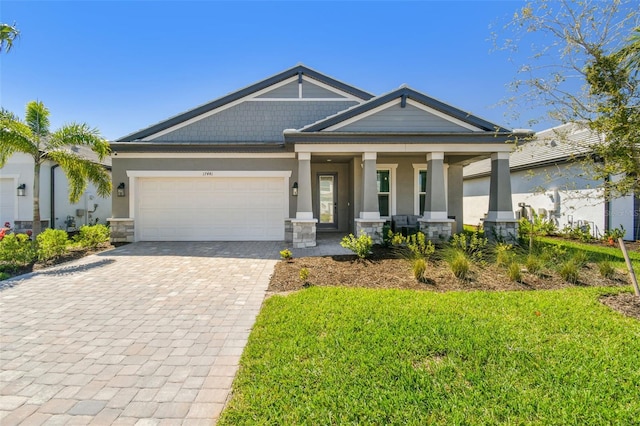 craftsman house with stucco siding, covered porch, decorative driveway, stone siding, and an attached garage