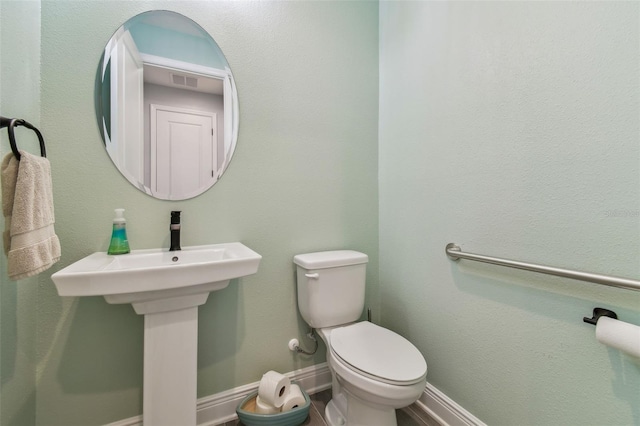 half bath featuring visible vents, toilet, and baseboards