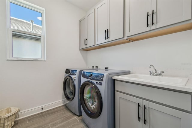 washroom with washer and clothes dryer, a sink, cabinet space, baseboards, and wood tiled floor