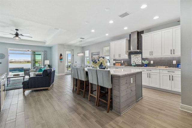 kitchen featuring wall chimney range hood, tasteful backsplash, visible vents, and light wood finished floors