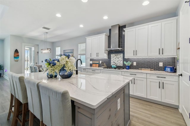 kitchen featuring visible vents, a kitchen bar, a sink, gas cooktop, and wall chimney range hood