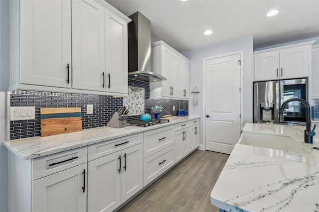 kitchen featuring a sink, appliances with stainless steel finishes, white cabinetry, wall chimney exhaust hood, and light wood-type flooring