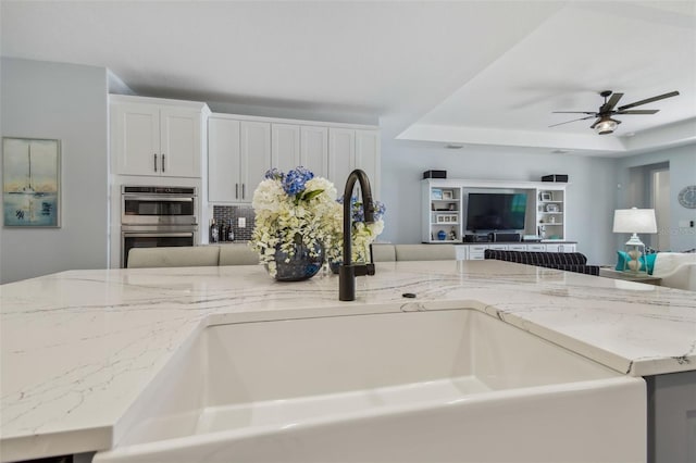 kitchen featuring a sink, light stone counters, open floor plan, and stainless steel double oven