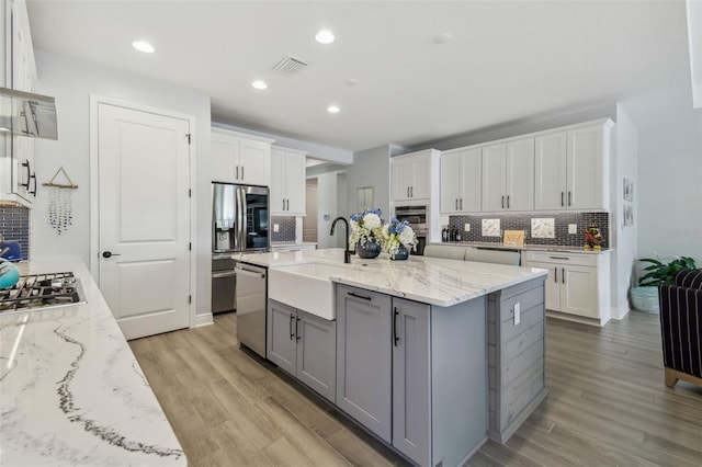 kitchen with visible vents, gray cabinetry, appliances with stainless steel finishes, light wood-style floors, and a sink