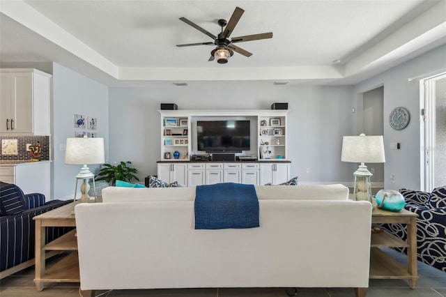 living area featuring ceiling fan, a tray ceiling, and wood finished floors