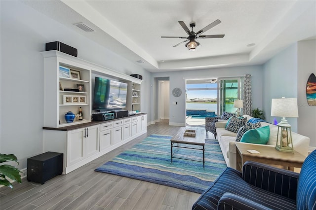 living area featuring a tray ceiling, a ceiling fan, baseboards, and light wood finished floors