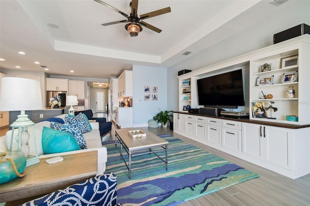 living room featuring recessed lighting, ceiling fan, a raised ceiling, and light wood-style floors