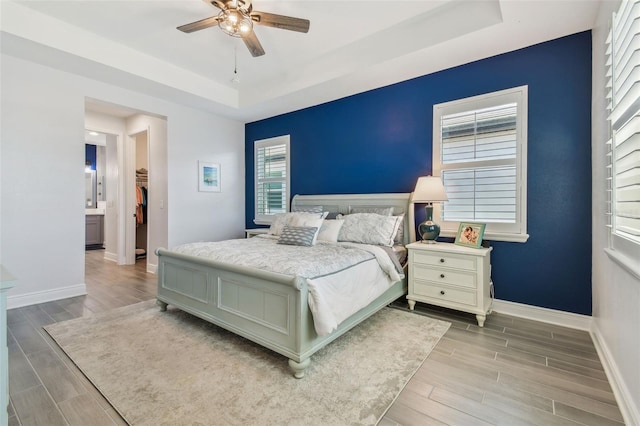 bedroom with a ceiling fan, a raised ceiling, baseboards, and wood tiled floor