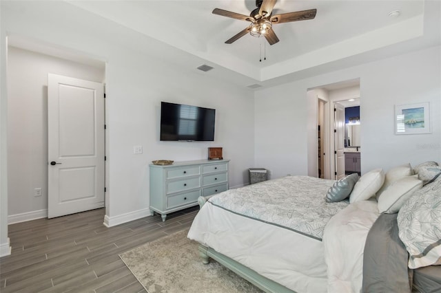 bedroom with visible vents, baseboards, wood tiled floor, a tray ceiling, and a ceiling fan