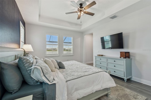 bedroom featuring wood finish floors, visible vents, baseboards, a raised ceiling, and ceiling fan