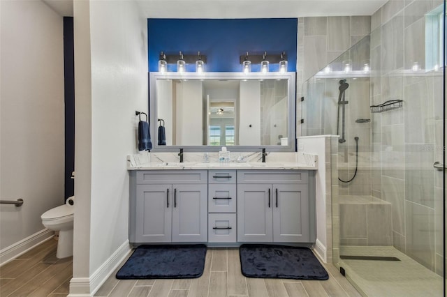 full bath with wood finish floors, tiled shower, double vanity, a sink, and toilet