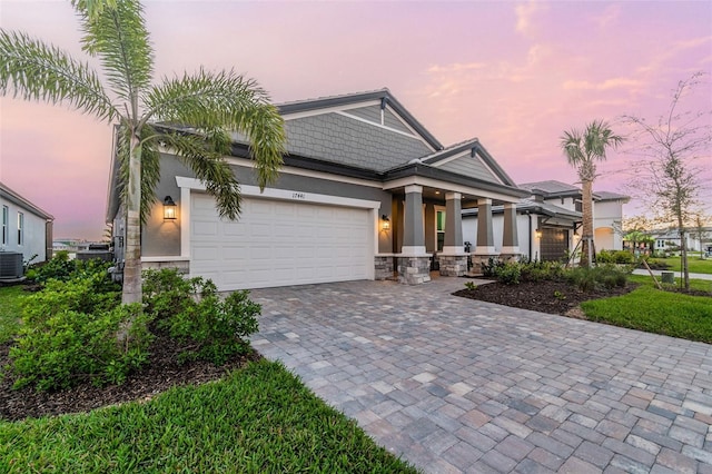 craftsman-style house with stucco siding, central AC unit, decorative driveway, stone siding, and an attached garage