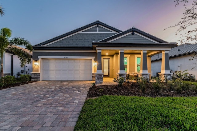 craftsman-style home featuring a porch, an attached garage, stucco siding, stone siding, and decorative driveway