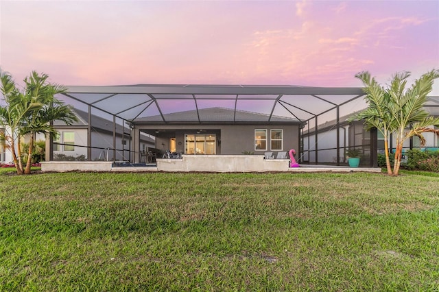 back of property at dusk with a patio, a lanai, a yard, and stucco siding