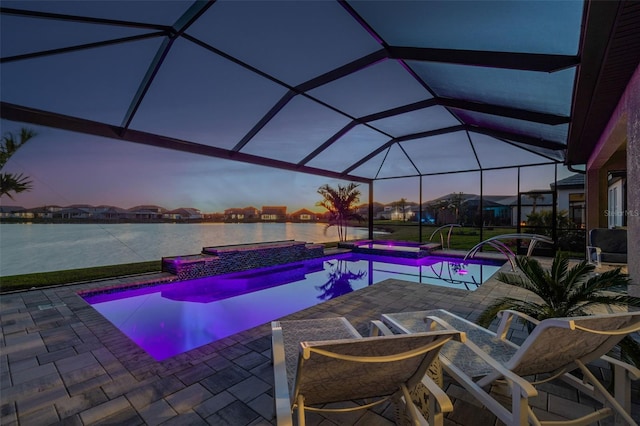 pool at dusk featuring glass enclosure, a pool with connected hot tub, and a patio