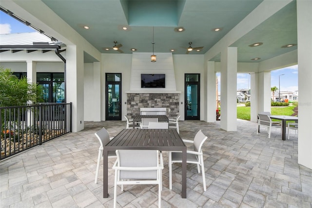 view of patio with ceiling fan, outdoor dining space, an outdoor fireplace, and fence