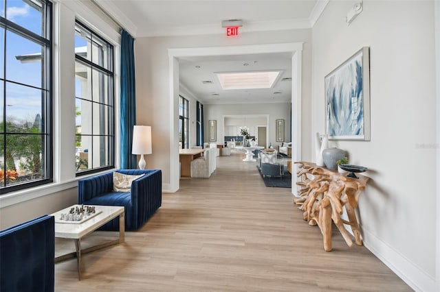 hall featuring baseboards, a skylight, crown molding, and light wood finished floors