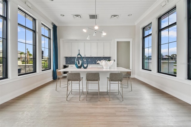 kitchen with a breakfast bar, light wood-style flooring, ornamental molding, white cabinets, and tasteful backsplash