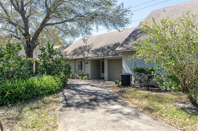 cape cod-style house with central air condition unit, stucco siding, driveway, and a shingled roof