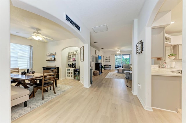 dining space with a ceiling fan, light wood-type flooring, arched walkways, and baseboards