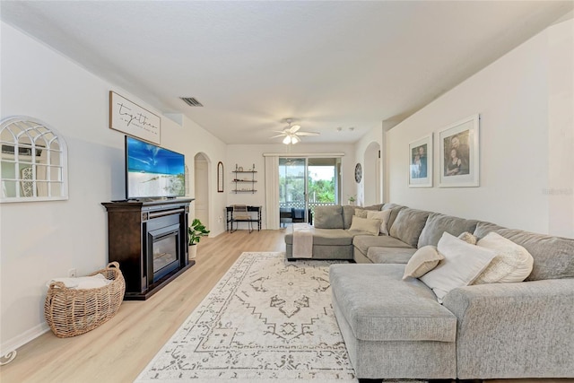 living room with visible vents, arched walkways, baseboards, a glass covered fireplace, and light wood-type flooring