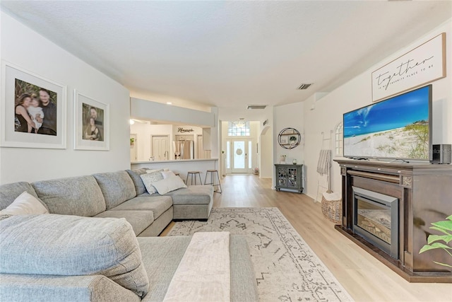 living room with light wood finished floors, visible vents, and a glass covered fireplace