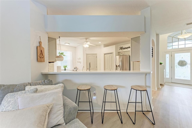 kitchen featuring arched walkways, a breakfast bar, light wood finished floors, light countertops, and stainless steel fridge with ice dispenser