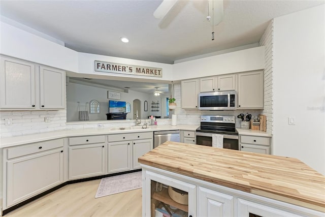 kitchen featuring tasteful backsplash, a ceiling fan, appliances with stainless steel finishes, wooden counters, and a sink