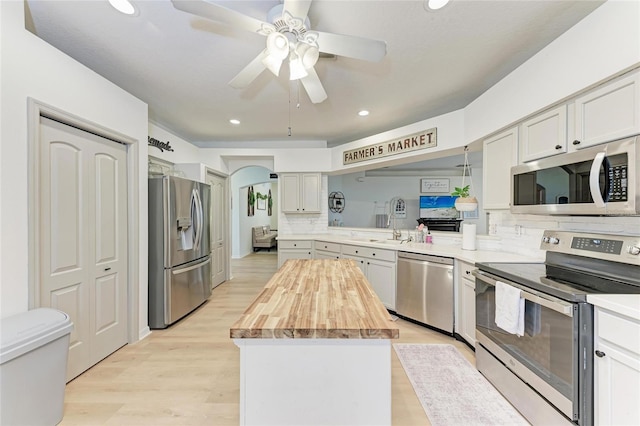 kitchen with light wood-style flooring, butcher block countertops, a sink, appliances with stainless steel finishes, and a center island