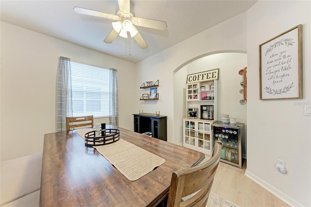 dining room with arched walkways, light wood-type flooring, a ceiling fan, and baseboards