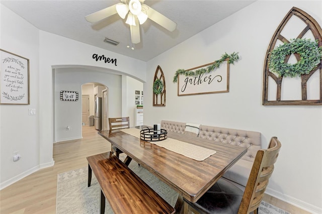 dining space featuring visible vents, arched walkways, a ceiling fan, baseboards, and light wood-style flooring