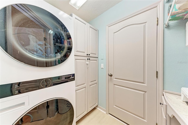 washroom with a textured ceiling, cabinet space, and stacked washer / drying machine