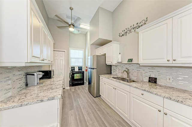 kitchen with a ceiling fan, a sink, freestanding refrigerator, and white cabinetry