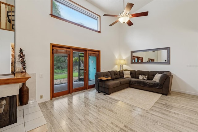 living room featuring a towering ceiling, light wood-style floors, baseboards, ceiling fan, and a tile fireplace