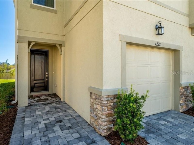 entrance to property with a garage, stone siding, and stucco siding